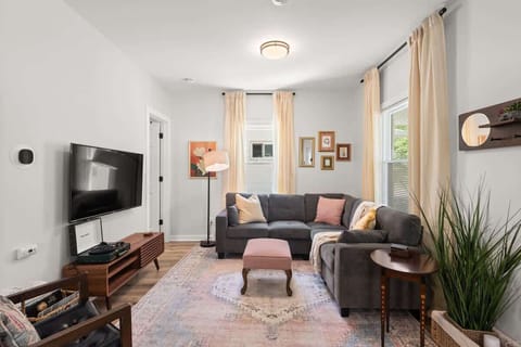 Bright living room w/ cozy seating, wall-mounted TV & large windows letting natural light pour in