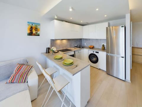 A kitchen and dining combo with a small table for two, fridge, and modern cabinets in bright lighting.