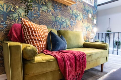 Snuggle up in this inviting corner of the living room, where comfort meets style. The plush, olive-green sofa adorned with vibrant cushions and a cozy throw is perfect for unwinding after a day of exploring the city. The chic wallpaper adds a touch o