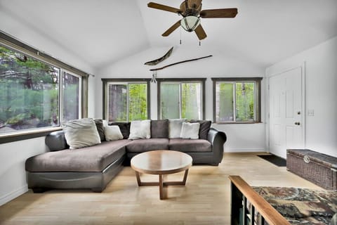 Bright living room with vaulted ceiling, large picture windows, and forest views.