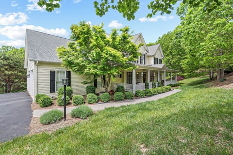 Inviting home with a spacious driveway, lush greenery, and a classic wraparound porch