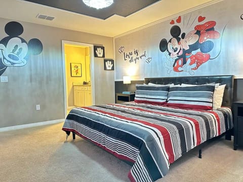 King bed with Mickey Mouse themed linens, en-suite bathroom, and plush carpeting.