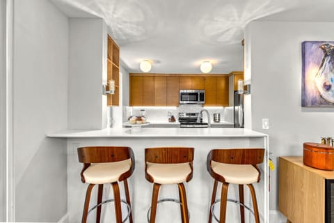 A wide kitchen passthrough opens to three neatly arranged bar stools, inviting casual conversation with a view into the heart of the home.