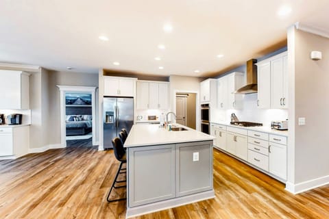 A modern kitchen features white cabinetry, stainless steel appliances, a central island with bar stools, and warm wooden flooring