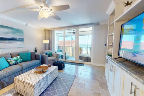 The spacious living room is designed for relaxation, featuring a comfortable sofa, a large flat-screen TV, & direct access to the beachfront balcony