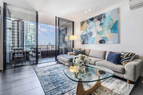 LIVING ROOM: A setting of quiet refinement, where open living flows seamlessly to a soft-hued sectional, a perch above the city where evenings naturally come to rest.