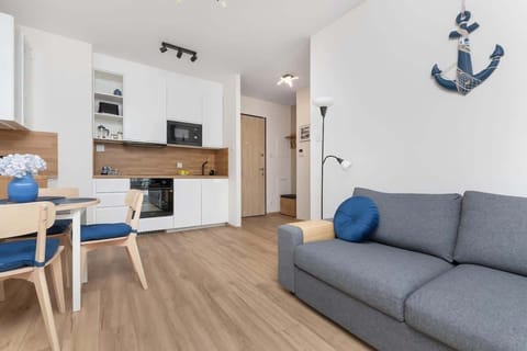 A cozy living room with a gray sofa, blue accent pillows, and a dining table near the kitchen.

