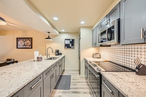 Modern kitchen with gray cabinets, stainless steel appliances, and granite countertops. A wall-mounted blackboard is above the coffee maker, with recessed lighting illuminating the space.