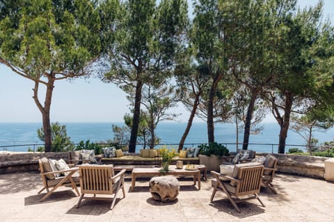 Sea-view terrace with wooden lounge furniture surrounded by pine trees.