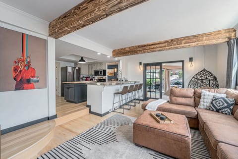 - Plush sectional sofa beneath rustic wood ceiling beams & natural light
- Fully equipped kitchen with breakfast bar seating, stainless steel appliances, & bold cabinetry
- Artistic wall features & a hanging chair add character to this stylish social hub