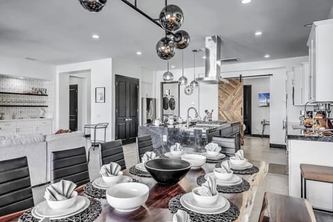 Gather in elegance at this stunning live-edge dining table set for twelve, perfectly placed in a seamless open floor plan that connects the kitchen, bar, and lounge areas. From the bold light fixtures to the black marble island and thoughtful decor, this space was designed to host memorable meals, celebrations, and conversations in modern luxury.