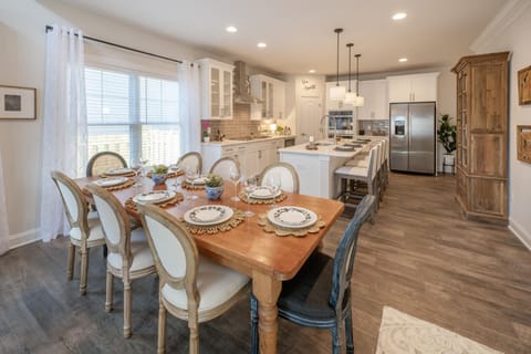 The dining room boasts a charming wooden table complemented by farmhouse-style high-back chairs with seating for 8.
