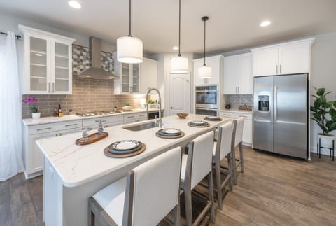 The image features a contemporary counter seating arrangement designed for four people. The sleek, quartz counter has a subtle gray veining, and it’s complemented by four high-backed, upholstered bar stools.