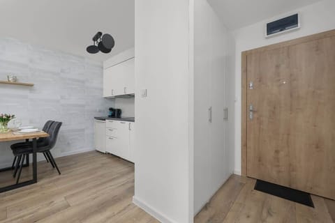 The kitchenette with white cabinets, wooden flooring, and a view of the entrance combines functionality with modern design.