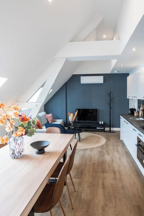 A beautifully integrated attic living space with a dining area leading into a cozy lounge and modern kitchen, all under sloped ceilings that enhance the airy and open feel of the room.