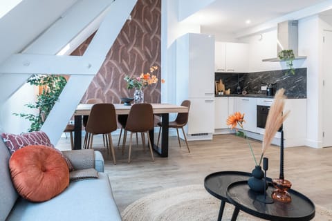 A stylish open living space with a modern dining area, cozy sofa, and a well-equipped kitchen, complemented by vibrant décor.