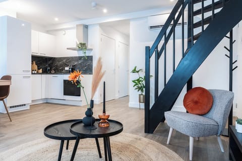 A well-designed living area with a cozy seating arrangement and a modern staircase, featuring minimalist decor and a warm ambiance.