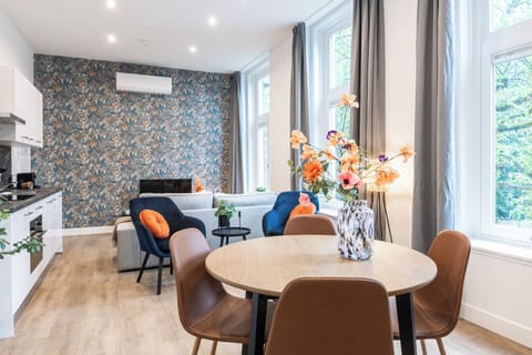 Bright and elegant studio apartment in Tilburg with floral wallpaper, cozy seating, and a charming dining area accented by a vase of vibrant flowers. Ideal for Bed en Koffie near Tilburg Centrum, and an affordable option for Efteling or Safaripark Beeksebergen stays.