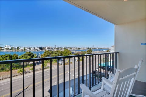 Balcony with white chairs overlooking a scenic waterfront and residential area below.