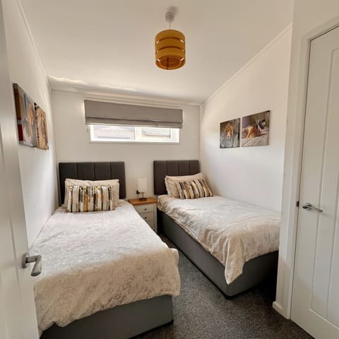 The twin bedroom features two single beds with a bedside cabinet and a table lamp placed between them. The room also includes a wardrobe with a shelf and hanging space for clothes.