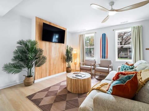 - Stylish living room with modern décor and natural wood accent wall   - Comfortable seating with bright pillows and indoor plants creating charm   - Smart TV and cozy setup designed for relaxing Airbnb nights  