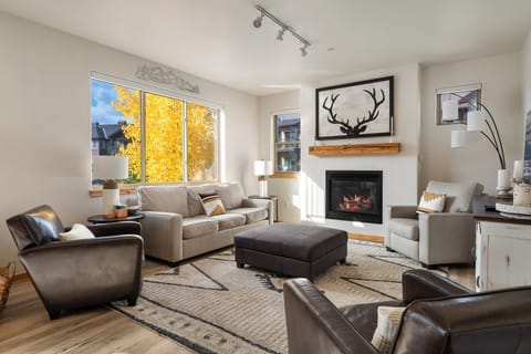 - Bright and inviting living room with modern furnishings and stylish antler art - Gas fireplace adds warmth and charm beneath cozy seating for everyone - Large windows and wood floors give this space a clean mountain modern feel