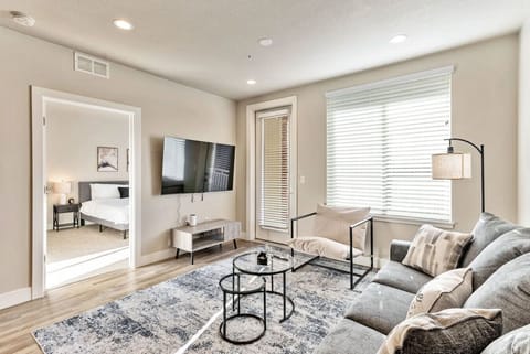 Bright living room w/ cozy sofa seating, wall-mounted TV & large windows bringing in natural light