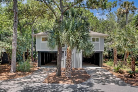 Cozy elevated duplex nestled under tall pines and palms, with shaded carports and a peaceful wooded setting.