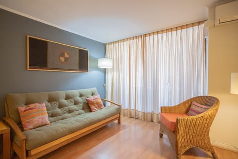 Relax in this cozy living space with a comfy futon and stylish wicker chair, bathed in natural light and accented with vibrant cushions.