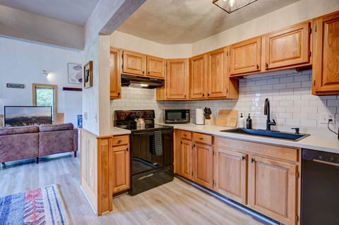 Fully equipped kitchen with warm wood cabinetry, modern black appliances, and all essentials for cooking a delicious family meal. Enjoy ample counter space, a coffee maker, and stylish subway tile.