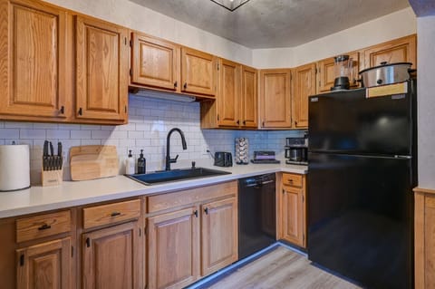 Fully equipped kitchen with warm wood cabinetry, modern black appliances, and all essentials for cooking a delicious family meal. Enjoy ample counter space, a coffee maker, and stylish subway tile.