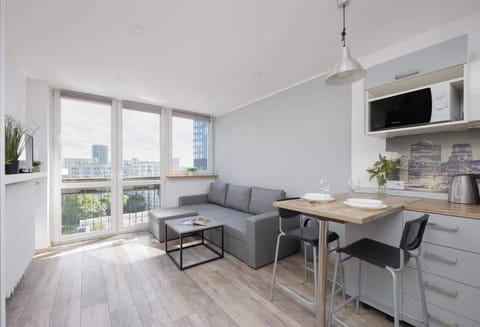 A bright living room with a dining table, gray sofa, and large windows allowing natural daylight to flood the space.