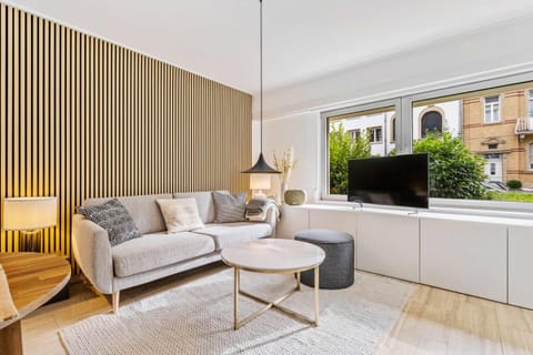 Cozy lounge space with elegant wood accents, a comfortable sofa, and a peaceful view toward the garden, perfect for unwinding after a day in Limpertsberg.