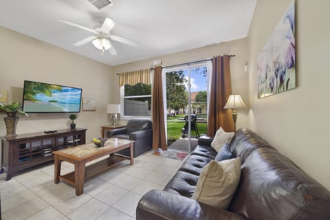 Cozy living room with leather sofas, flat-screen TV, and patio access to a lush garden view.