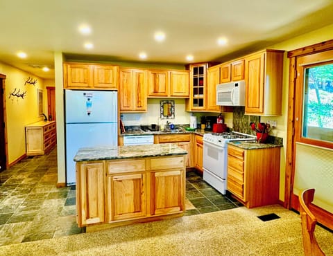 The kitchen is open with views out the deck door of the trees & Village beyond.