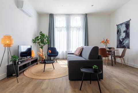 A contemporary living area with a plush sofa, chic chairs, sleek round tables, a TV unit, and natural accents, all enhanced by warm hues and lush greenery, seamlessly linking to the dining space.

Apart-Hotel – close to the university, city center, Efteling & Safaripark Beekse Bergen. Equipped with a new kitchen and a luxury bathroom.