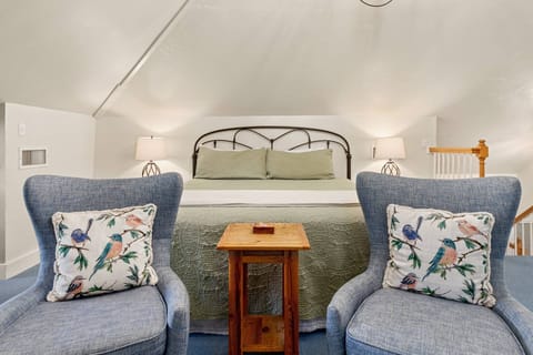 Cozy loft retreat with a king bed, comfy chairs, and charming bird-themed pillows under vaulted ceilings.