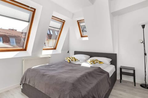 A bedroom under a sloped ceiling featuring a cozy bed with grey and white linens. Two skylight windows let in plenty of natural light.