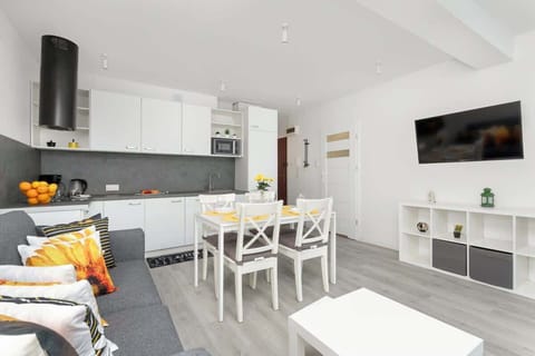 A white kitchen and dining area with wooden flooring and modern furnishings. The open layout connects seamlessly with the living space.