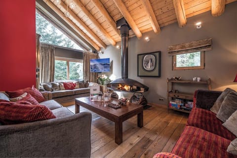 Relax in this cozy living room featuring plush seating, vibrant red accents, and a rustic wooden ceiling. Large windows flood the space with natural light, creating a warm and inviting atmosphere perfect for unwinding after a day of exploring.