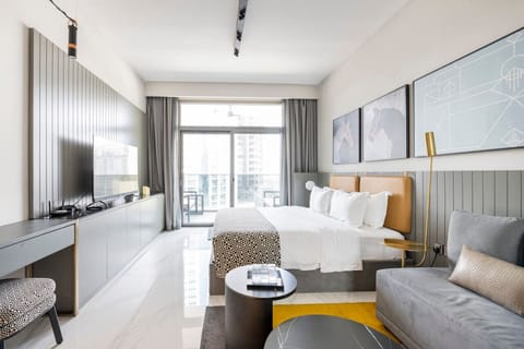 Elegant studio apartment at MAG 318, Business Bay. Features a cozy bed, stylish seating area, flat-screen TV, chic decor, and a balcony with city views. Ideal for a vacation rental or short-term rental in Dubai.