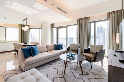 Spacious living room of a luxury apartment in Address Harbour Point Tower 1, Dubai Creek Harbour. Features modern furniture, plush beige sofas with blue cushions, glass coffee table, large windows offering city views, and abundant natural light.