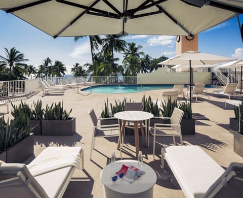 Lounge poolside under umbrellas with palm-framed island skies.