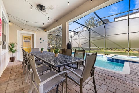 Spacious outdoor dining area with elegant seating, perfect for hosting gatherings - Covered patio with string lights, creating a cozy ambiance for evening events - Scenic view of the private pool and backyard through a screened enclosure