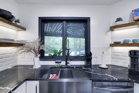 Sleek kitchen sink with black marble, wood shelves, and modern black fixtures.