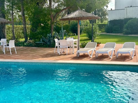 Pool area with sun loungers, outdoor table and garden surrounded by pine trees.