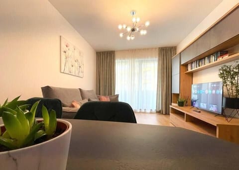 Spacious living room featuring an extensible sofa with decorative pillows, room darkening shades, multi-language library, plants, smart TV with Netfliix, dining table, and free Wi-Fi