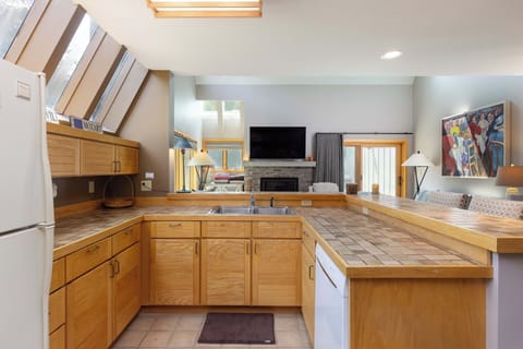 A spacious kitchen with wooden cabinets, a tiled countertop, and appliances including a refrigerator and dishwasher. Sunlight pours in through skylights, illuminating the open-concept living area.