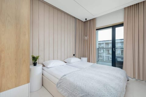 A serene bedroom with a double bed, minimalist decor, and large windows. Soft wooden tones create a calming atmosphere.