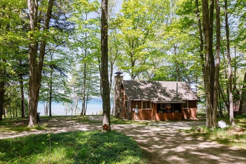 A charming cabin with a screened porch nestled among trees near a sparkling lake.